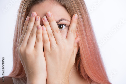 Young woman covers face with her hands and peep through her fingers