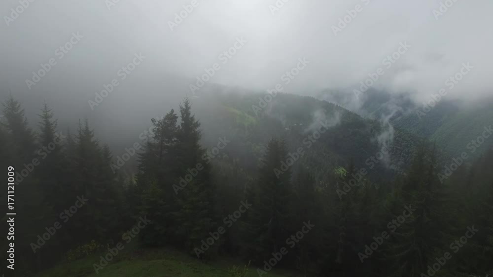Flight over mountain valley before the storm - heavy clouds float over wooded hills and small mountain village on the horizon. Adventure in the mountains. Flight over mountain valley before the storm - heavy clouds float over wooded hills and small mountain village on the horizon. Adventure in the mountains.