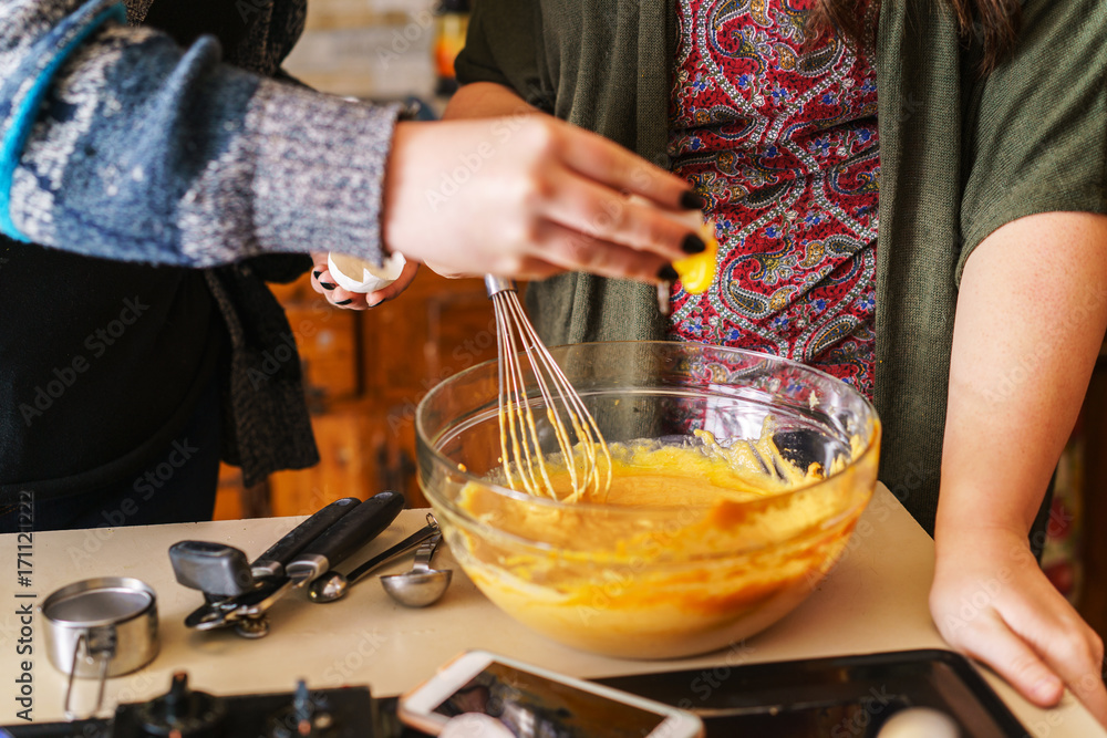 two girls following pumpkin pie recipe for halloween - adding egg yolks to batter in bowl two girls following pumpkin pie recipe for halloween - adding egg yolks to batter in bowl