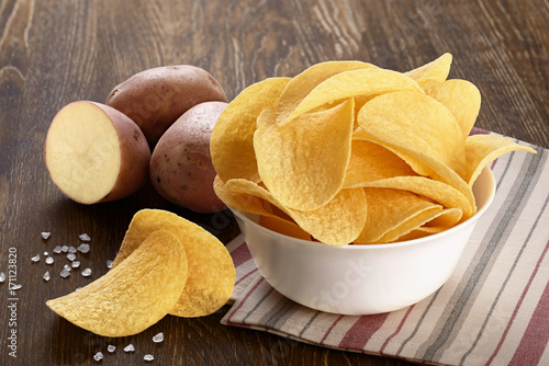 Potato and bowl with potato chips on a wooden background