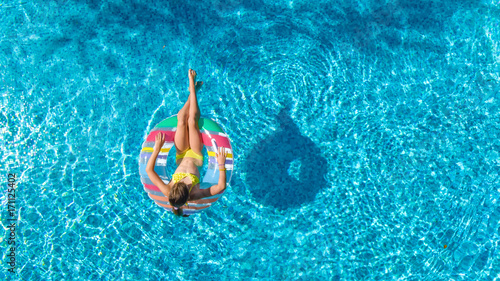 Aerial view of girl in swimming pool from above, kid swim on inflatable ring donut and has fun in water on family vacation 