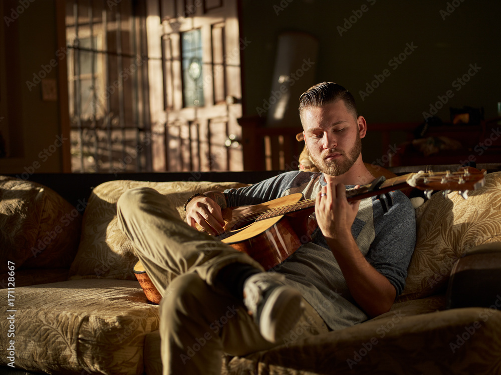man playing guitar on sofa at home man playing guitar on sofa at home