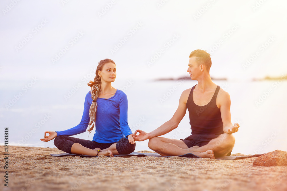 Couple is practising yoga meditatin pose at tropical sunrise sea background.