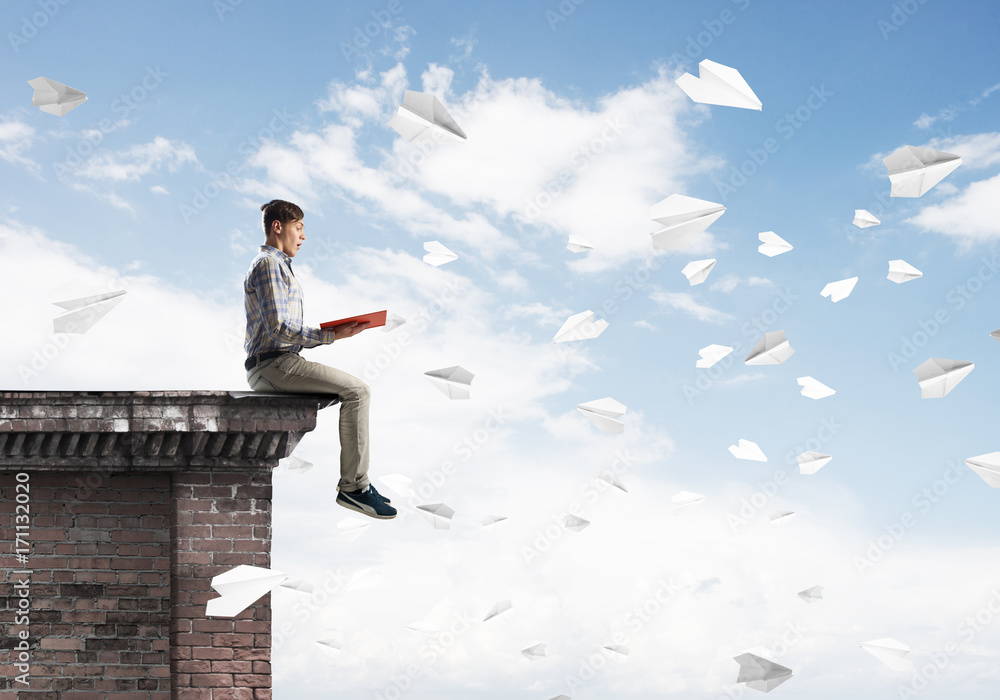 Handsome student guy on roof edge reading book and paper planes fly around Handsome student guy on roof edge reading book and paper planes fly around