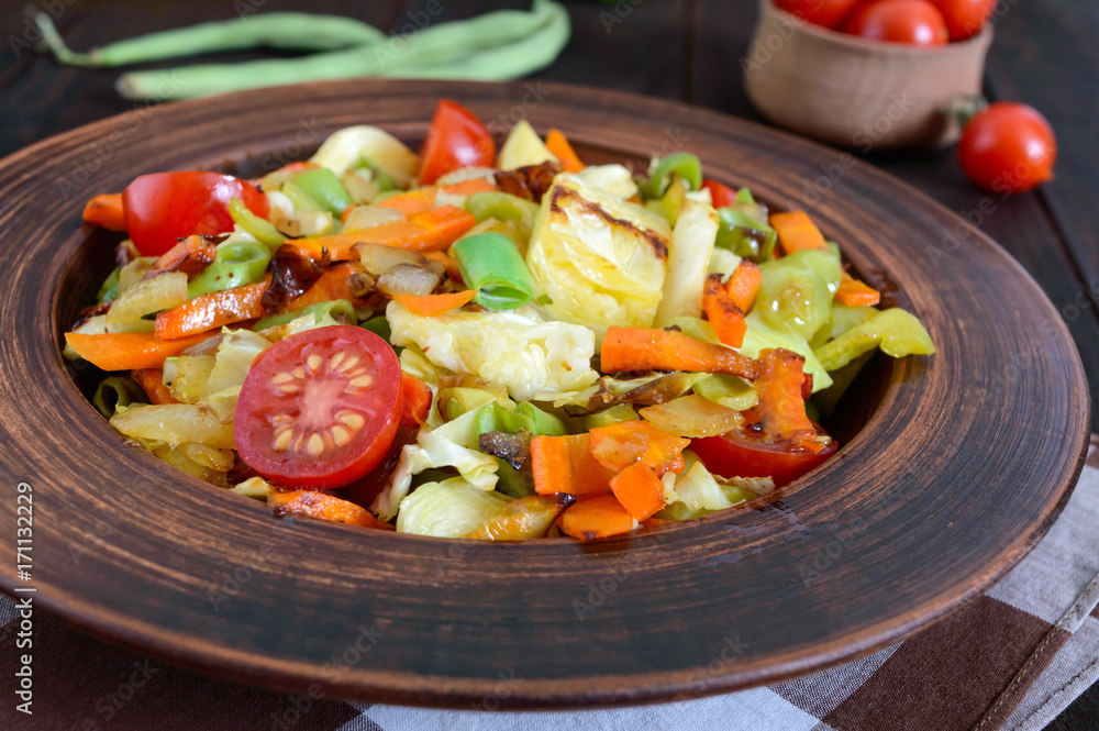 Vegetable stew of cabbage, green beans, carrots, tomatoes, onions, sweet peppers in a clay bowl on a dark wooden background. Warm salad. Vegetarian cuisine