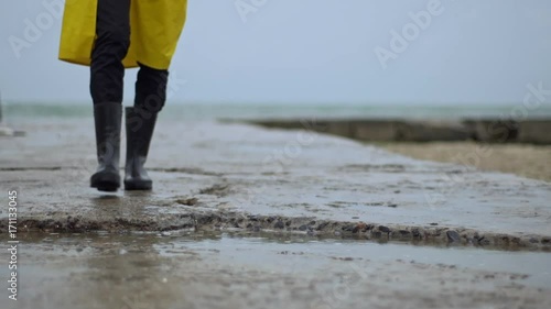 Person walking toward pier rain boots steps in puddle closeup photo