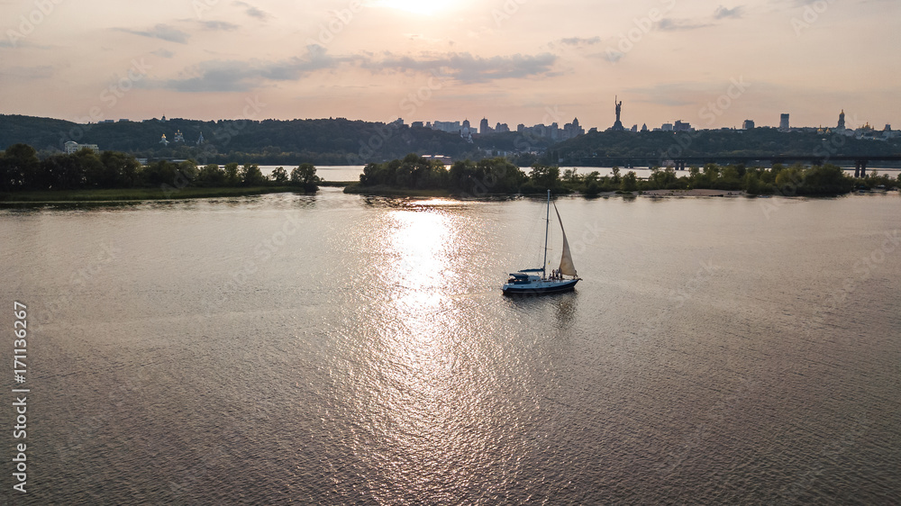 Naklejka premium Aerial view of Kiev city skyline on sunset, yacht sailing in Dnieper river from above, Kyiv, Ukraine 