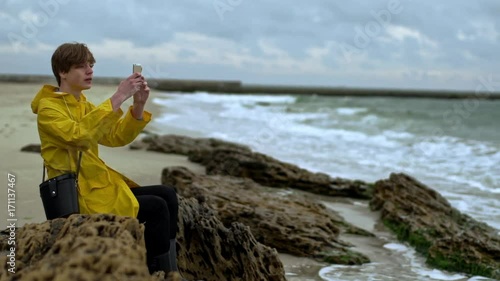 Young man sitting on shore filming waves phone slow motion