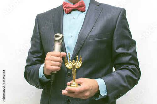 Man in suit with microphone in hand presenting an golden award to someone. The award ceremony. Success. Gratitude concept. Showman. photo