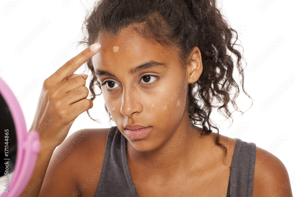 a young dark skinned woman applies a liqiud foundation on her face