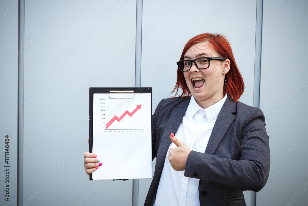 Business concept of success and growth. A successful woman boss, in suit and wearing glasses, holds a tablet with charts of growth and achievements. With place for text. Chef Day, Boss Day Business concept of success and growth. A successful woman boss, in suit and wearing glasses, holds a tablet with charts of growth and achievements. With place for text. Chef Day, Boss Day