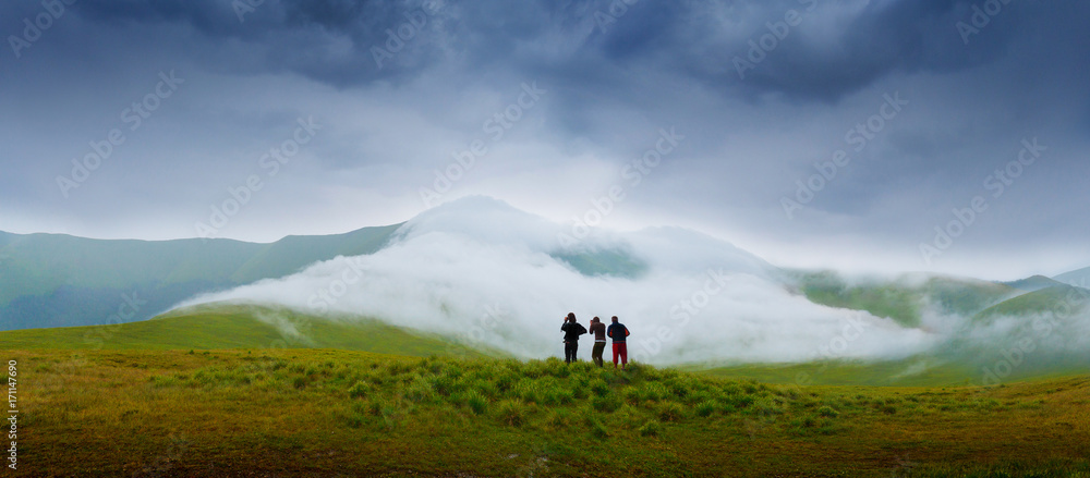 Hiking campers photographing a natural phenomenon - the clouds that roam the mountains. Concept theme: nature, weather, tourism, extreme, healthy lifestyle, adventures. Unrecognizable persones.