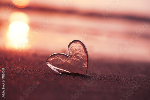 clear glass heart on  sand beach with sunrise sun light