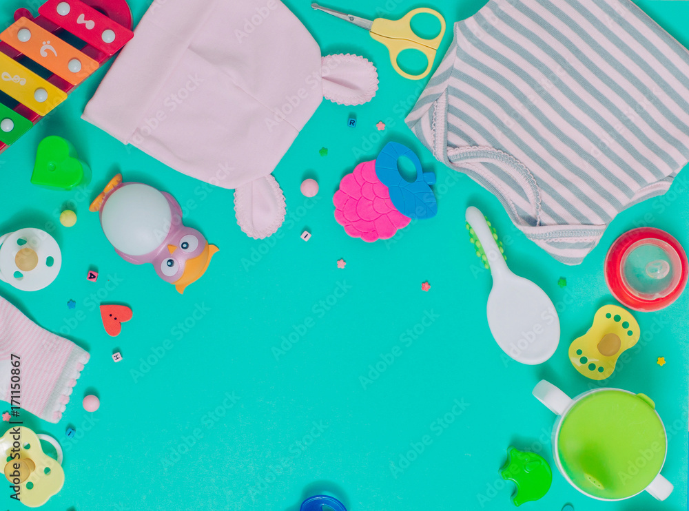 Naklejka premium Baby clothes, soother, spoon, brush and toys over green background