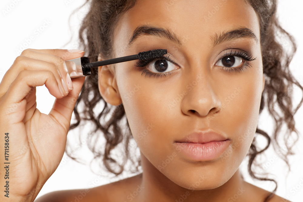 a young dark skinned woman applying a mascara to her eyelashes