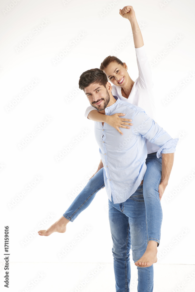 Happy couple having fun against white background.. Young man giving piggy back to her girlfriend. Happy couple having fun against white background.. Young man giving piggy back to her girlfriend.