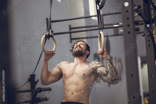 Muscle-up exercise young man doing intense cross fit workout at the gym on gymnastic rings photo