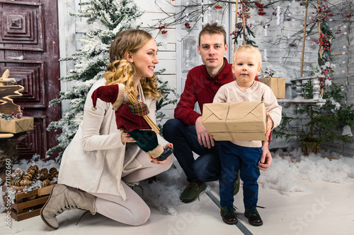 Portrait of happy young family. Parents surprising his little son with Christmas gift. Pretty glad boy hold in hands his present. Concept of Christmas and New Year