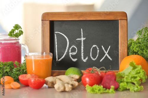 Small chalkboard with word DETOX, fresh juices and ingredients on table