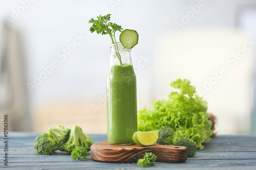 Glass bottle with fresh green juice and ingredients on table