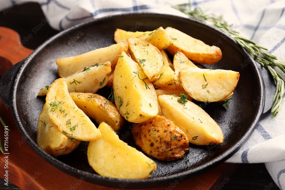 Frying pan with delicious baked potato wedges on wooden board, close up Frying pan with delicious baked potato wedges on wooden board, close up
