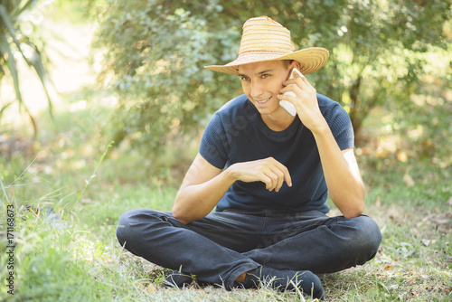 Young caucasian man, modern farm boy, talking on his phone and enjoying a sunny day in the countryside