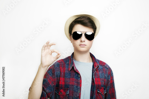 Portrait of a handsome boy with eyeglasses and hat and shows ok sign 