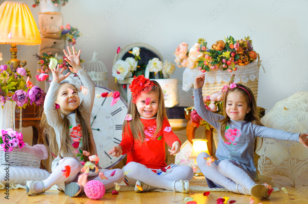 three little girls having fun sitting on the floor, throwing petals and laughing