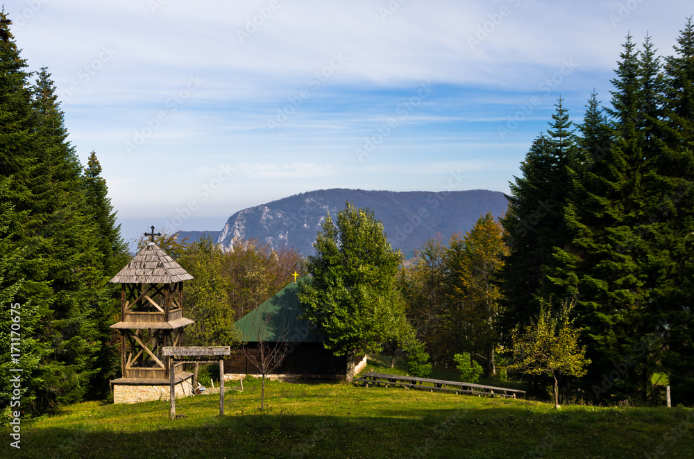 Viewpoint on a landscape of mount Bobija, meadow in front of an old wooden church surrounded by tall fir trees with rocky peaks in backgound, west Serbia