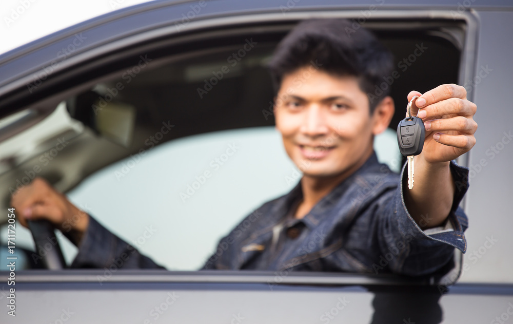 Handsome young  man is smiling, looking at camera and showing car keys while sitting in the car.