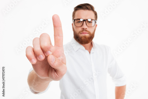 Young serious bearded man in eyeglasses showing forefinger