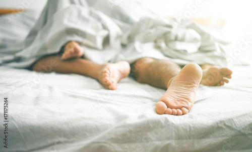 Close up of male and female feet on a bed - Loving couple having sex under under white blanket in the bedroom photo