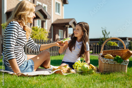 Caring mother giving her daughter a sandwich on picnic