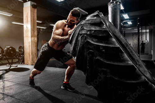 Shirtless man flipping heavy tire at crossfit gym photo