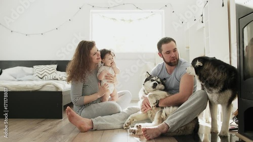 Father, mother, little daughter sits on the floor with dog near chimney with boiler.