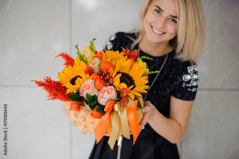Fototapeta premium Autumn flowers in hands of woman. Pumpkin, sunflowers and other flowers