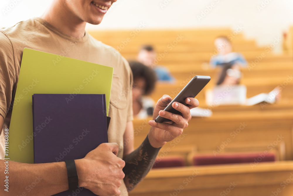 Happy guy typing message on smartphone in lecture hall