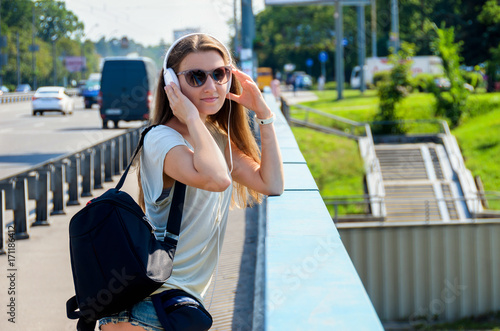 Beautiful slim stylish girl student stands on the car bridge and listens to music © Alona Dudaieva