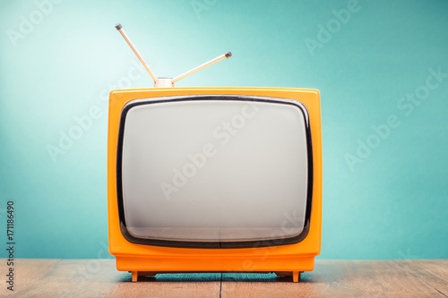 Retro old orange TV set receiver on wooden table front gradient mint green wall background. Vintage style filtered photo