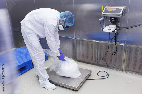 Specialist in the protected clothing and mask weighs the produced medical preparations on special scales.