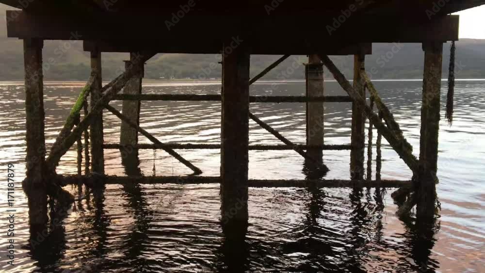 Waters flow and ripple underneath the wooden dock of Loch Sunart 4K as the sun sets in the sky Waters flow and ripple underneath the wooden dock of Loch Sunart 4K as the sun sets in the sky