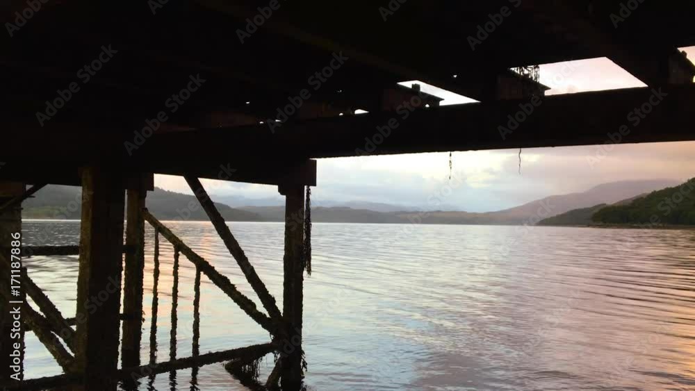 Waters flow and ripple underneath the wooden dock of Loch Sunart 4K as the sun sets in the sky Waters flow and ripple underneath the wooden dock of Loch Sunart 4K as the sun sets in the sky