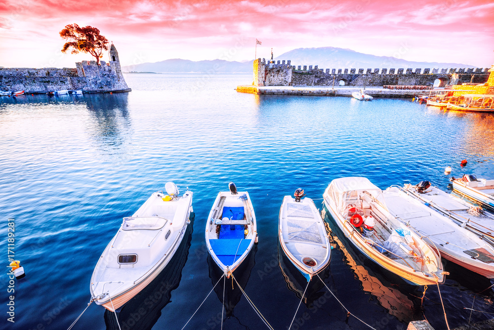 Nafpaktos bay, Greek small town, famous and popular travel destination with old castle at the bank of sea. Row of motor boats anchored in marine. Sunrise beautiful scenery.