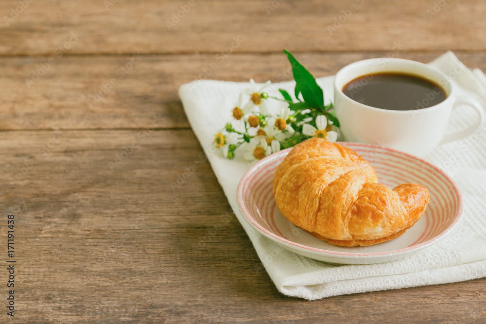 Homemade croissant on plate served with black coffee or americano. Delicious and quick breakfast with fresh croissant and coffee. Croissant and black coffee for breakfast on wood table with copy space Homemade croissant on plate served with black coffee or americano. Delicious and quick breakfast with fresh croissant and coffee. Croissant and black coffee for breakfast on wood table with copy space