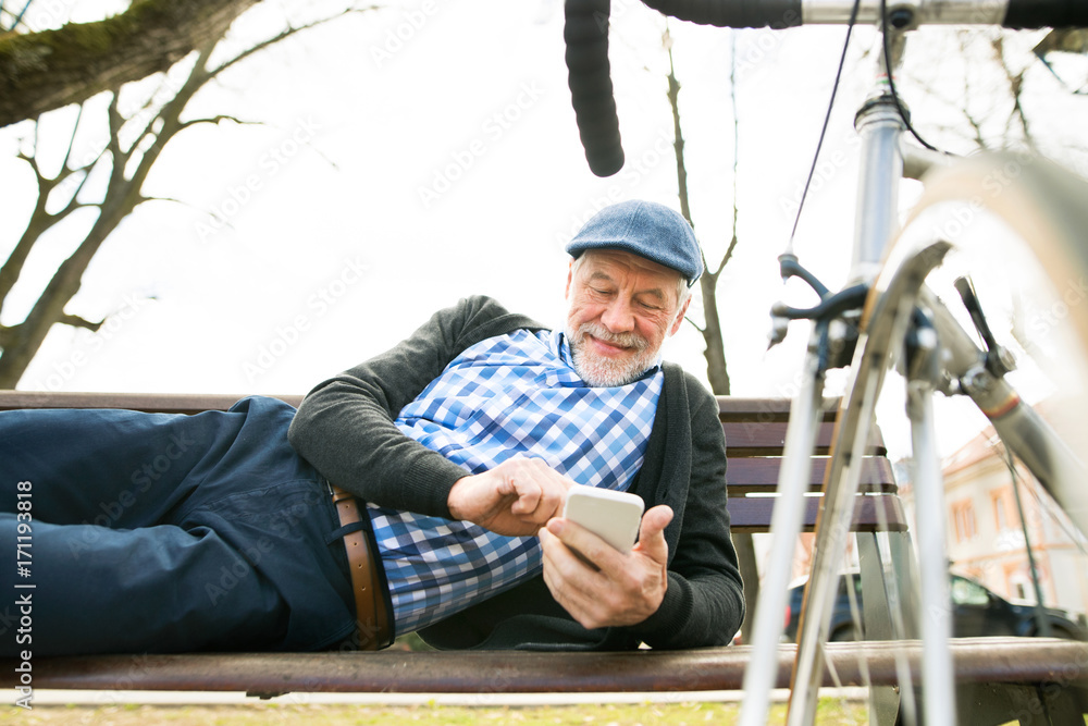 Senior man with bicycle in town, holding smart phone, texting Senior man with bicycle in town, holding smart phone, texting