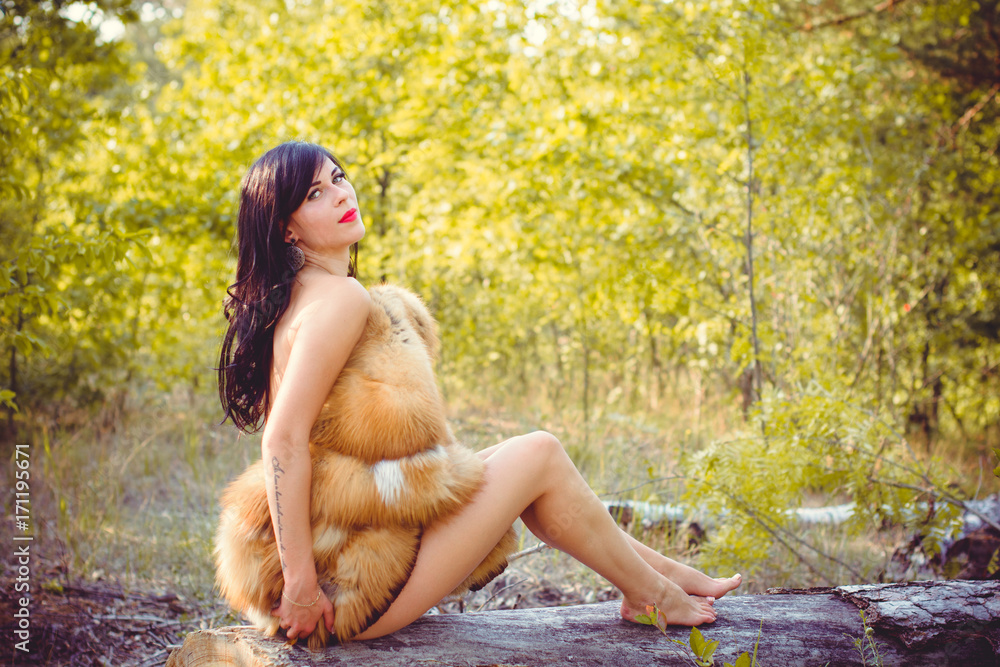 Young in luxurious furs with a naked body in the forest against a background of nature. Beautiful lady posing near trees in a fur coat Stock Photo | Adobe Stock