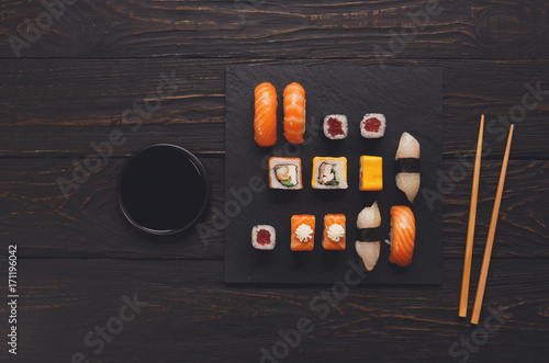 Set of salmon sushi and rolls on black wood background, top view