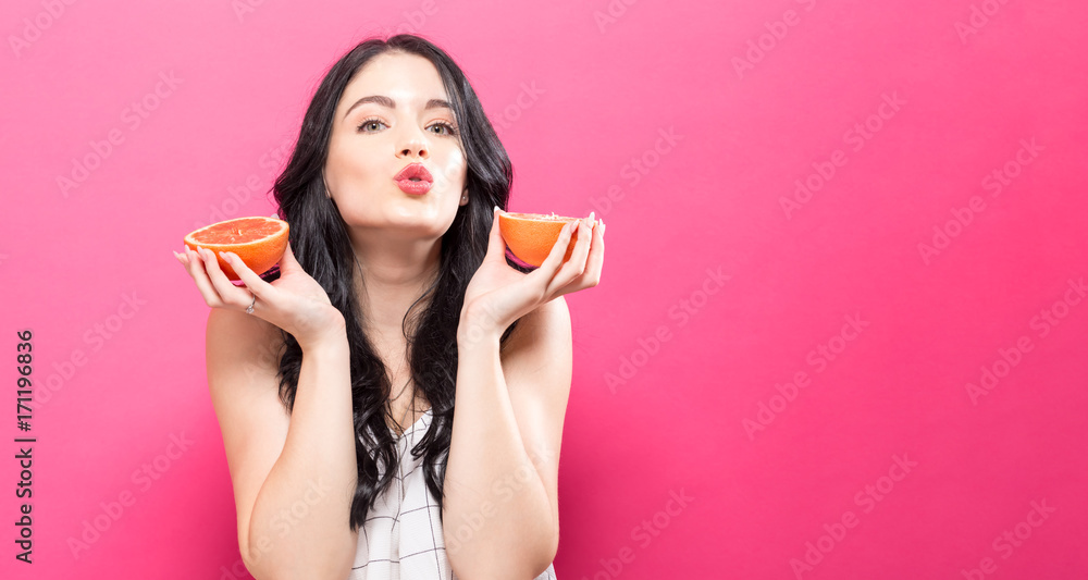 Happy young woman holding oranges on a pink background Happy young woman holding oranges on a pink background