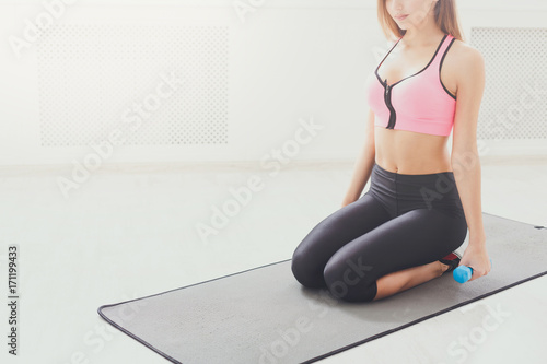 Fitness woman with dumbbells sitting on mat