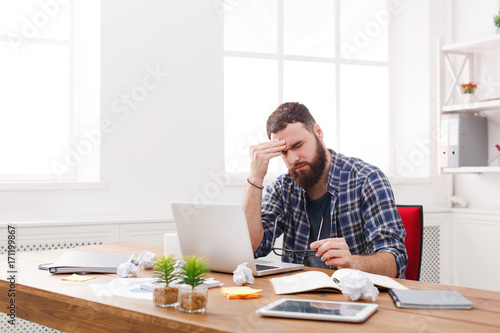 Tired stressed male programmer with laptop in modern white office © Prostock-studio